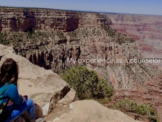 Alicia Ramirez sits on the edge of a canyon overlook, gazing at the expansive Grand Canyon landscape under clear blue skies, with the text "My experience as a counselor" overlayed.