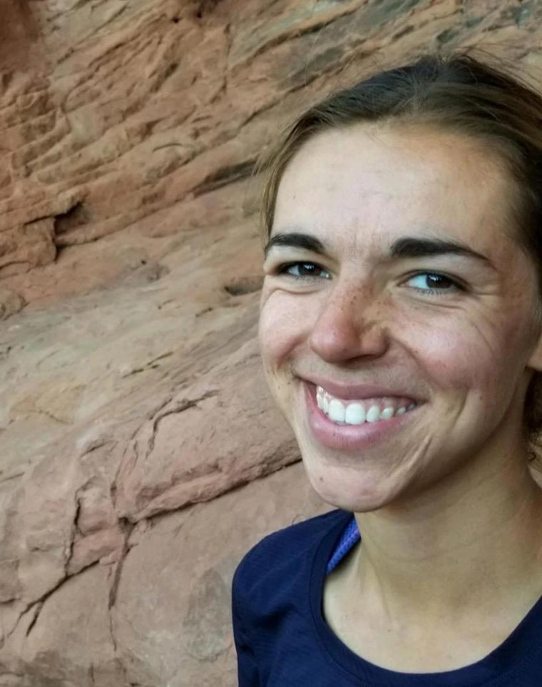 Katie Portman smiling in front of a red rock formation, wearing a navy athletic shirt.