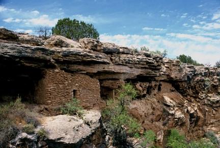 Ancient cliff dwellings built from stone are situated around an ancient pool of water. 