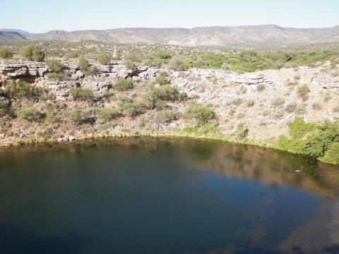 A massive natural spring is surrounded by multiple small cliff dwellings. 